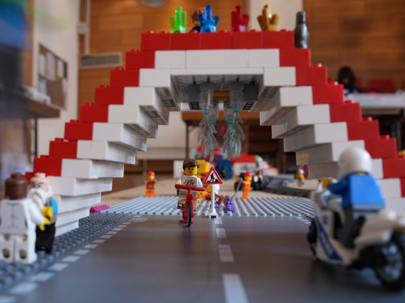 Eine Brücke aus Legosteinen unter den ein Legomensch auf einem Roller hindurchfährt