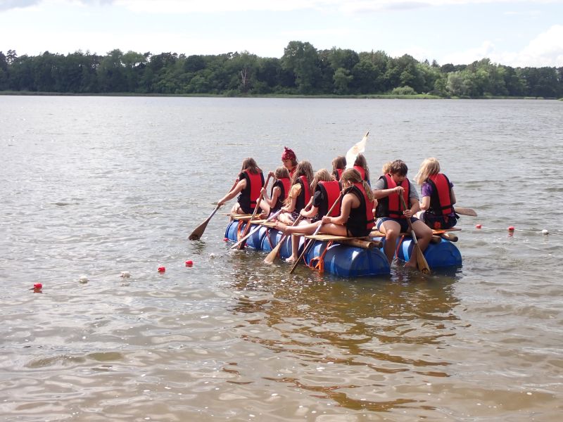Kinder padeln auf einem selbstgebauten Floß auf dem Brahmsee