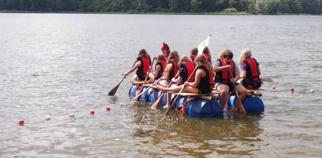 Kinder padeln auf einem selbstgebauten Floß auf dem Brahmsee
