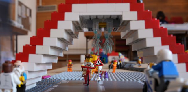 Eine Brücke aus Legosteinen unter den ein Legomensch auf einem Roller hindurchfährt
