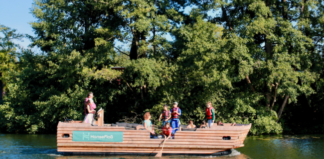 Hansefloß auf der Wakenitz. Kinder in Rettungswesten spielen mit einem Kescher.