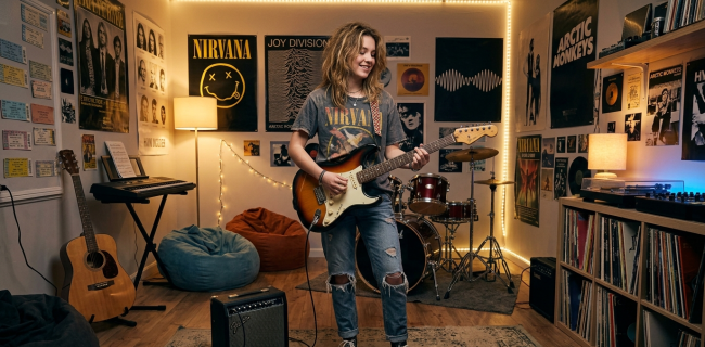 Ein lächelnder Junge spielt e-Gitarre in einem Musikzimmer